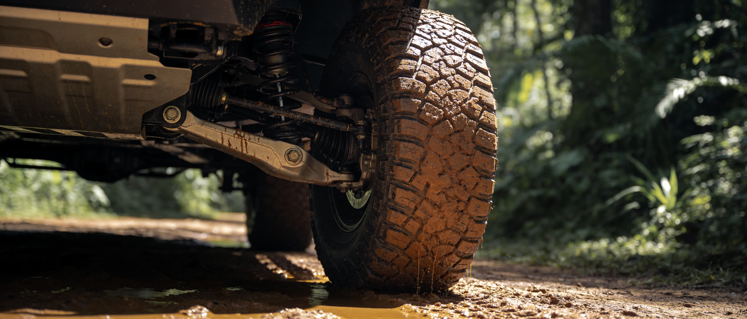 Rueda embarrada y suspensión de un 4x4 sobre barro, selva al fondo